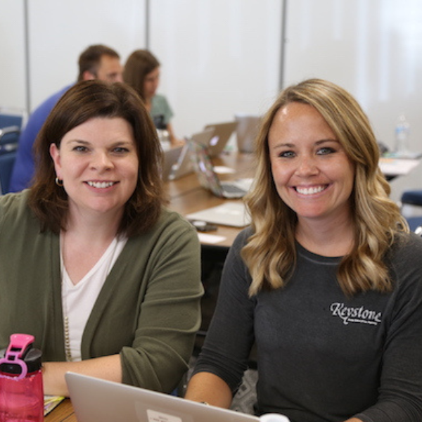two women smiling while sitting at a table with a laptop